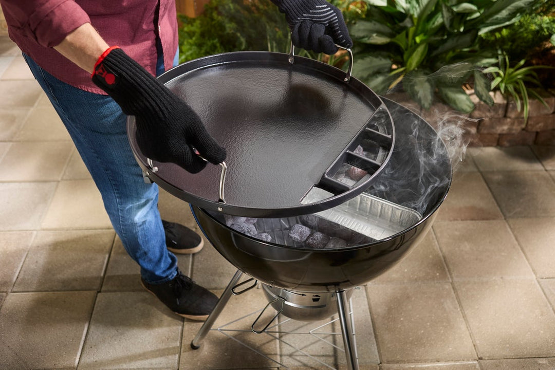 Weber Full-Size Griddle being fitted on a Weber charcoal barbecue in a garden